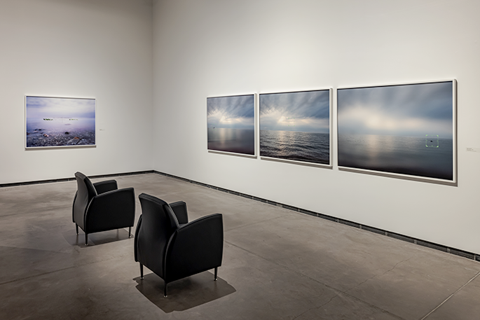 Two black chairs facing a wall with three photographs of water hanging