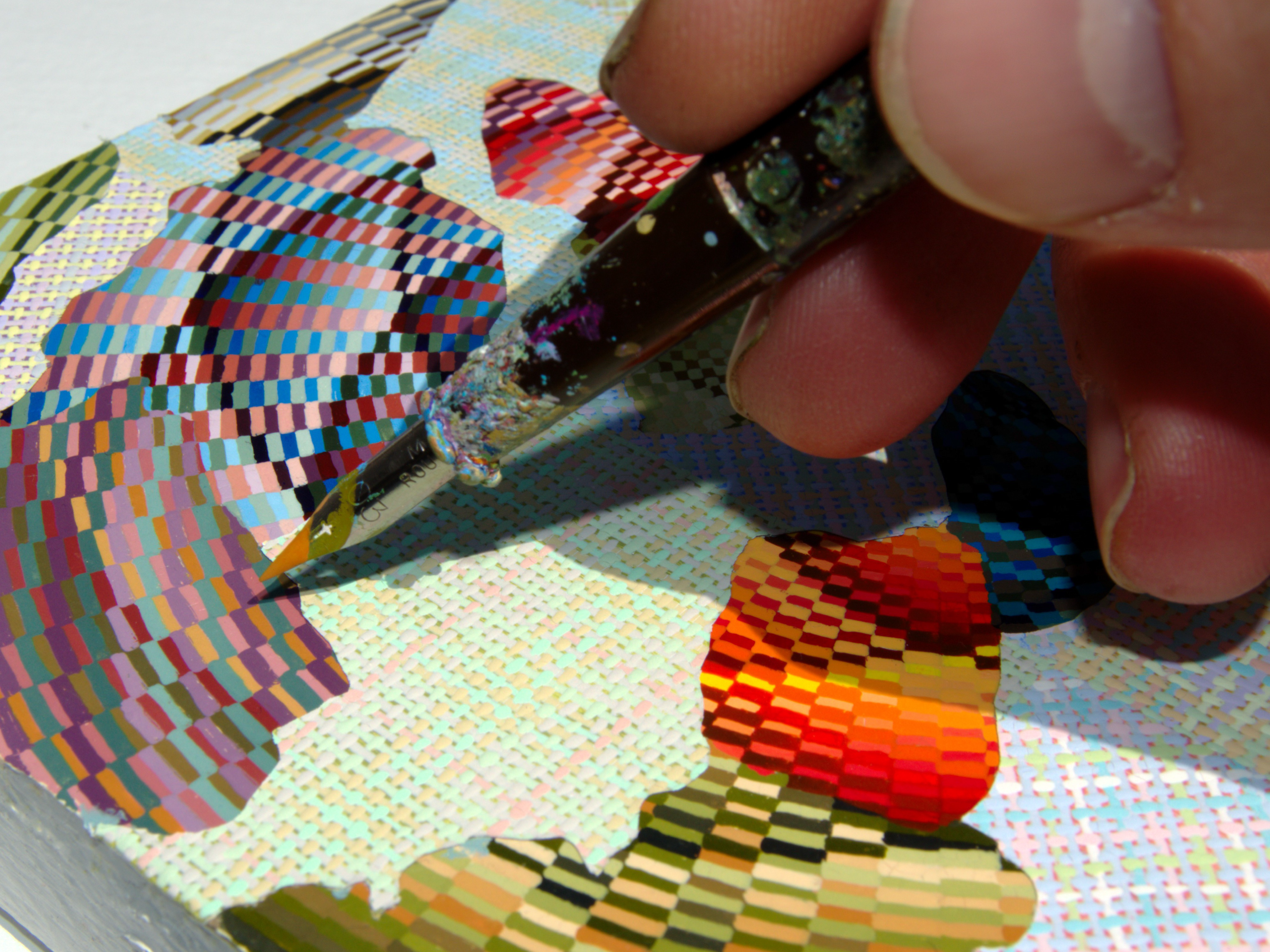 A close-up of a hand using a paintbrush to create a colorful, pixel‑like acrylic pattern on a canvas.