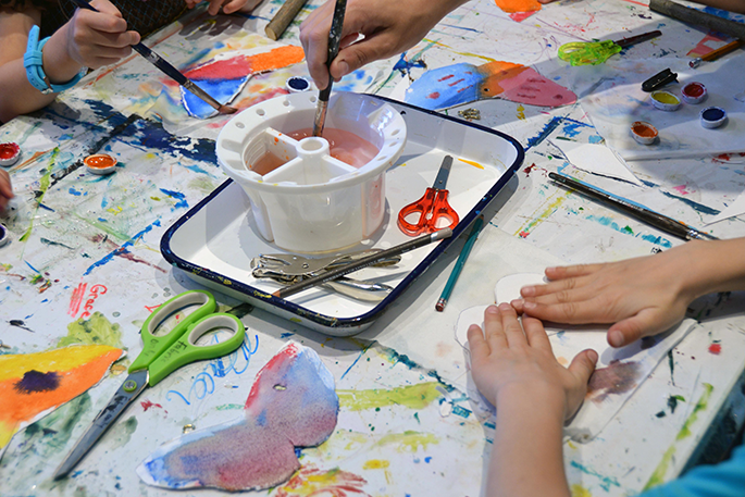 Children holding paintbrushes and painting paper butterflies