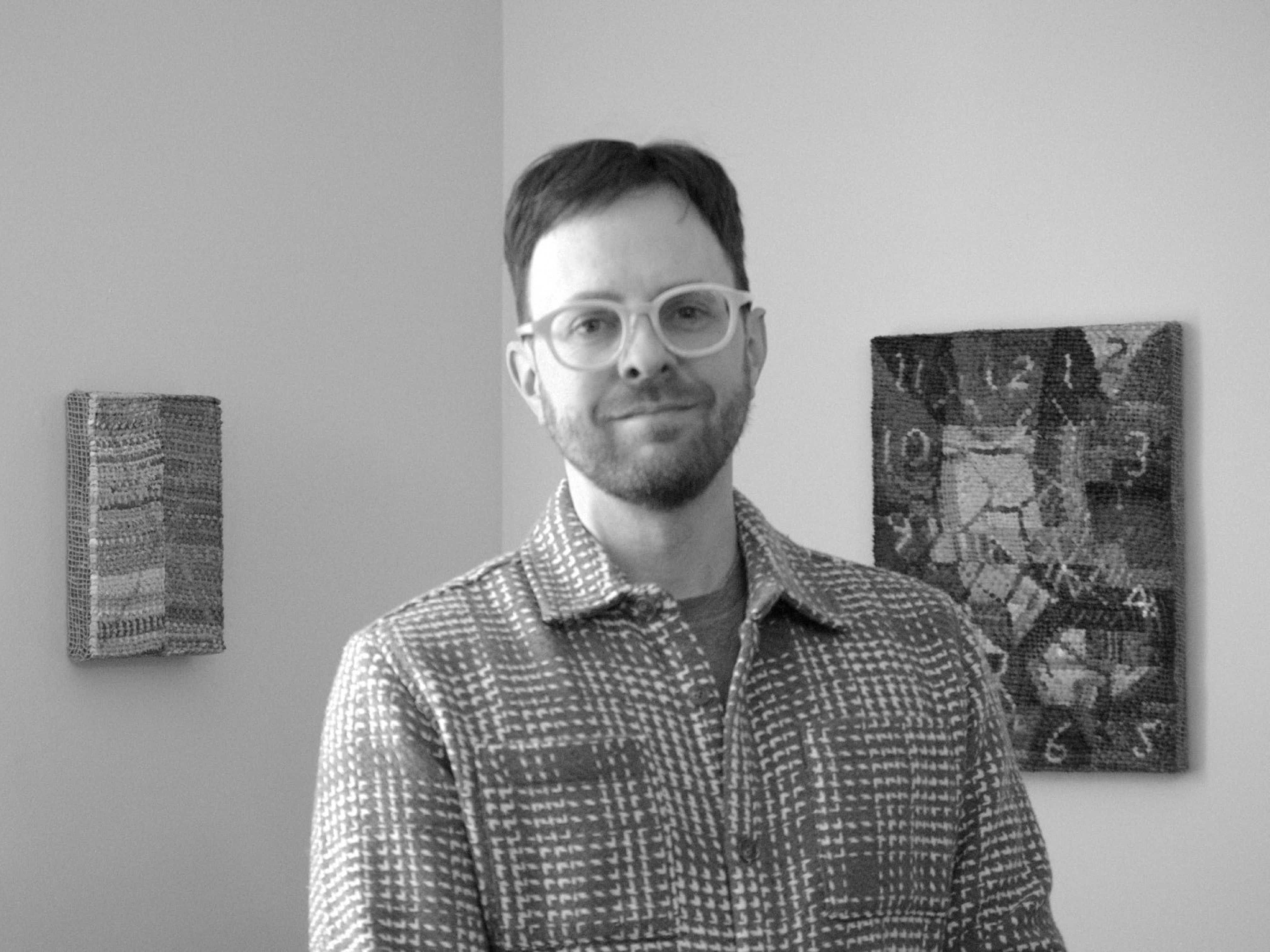 Mark Stebbins standing in front of some of his artwork. The photo is black and white.