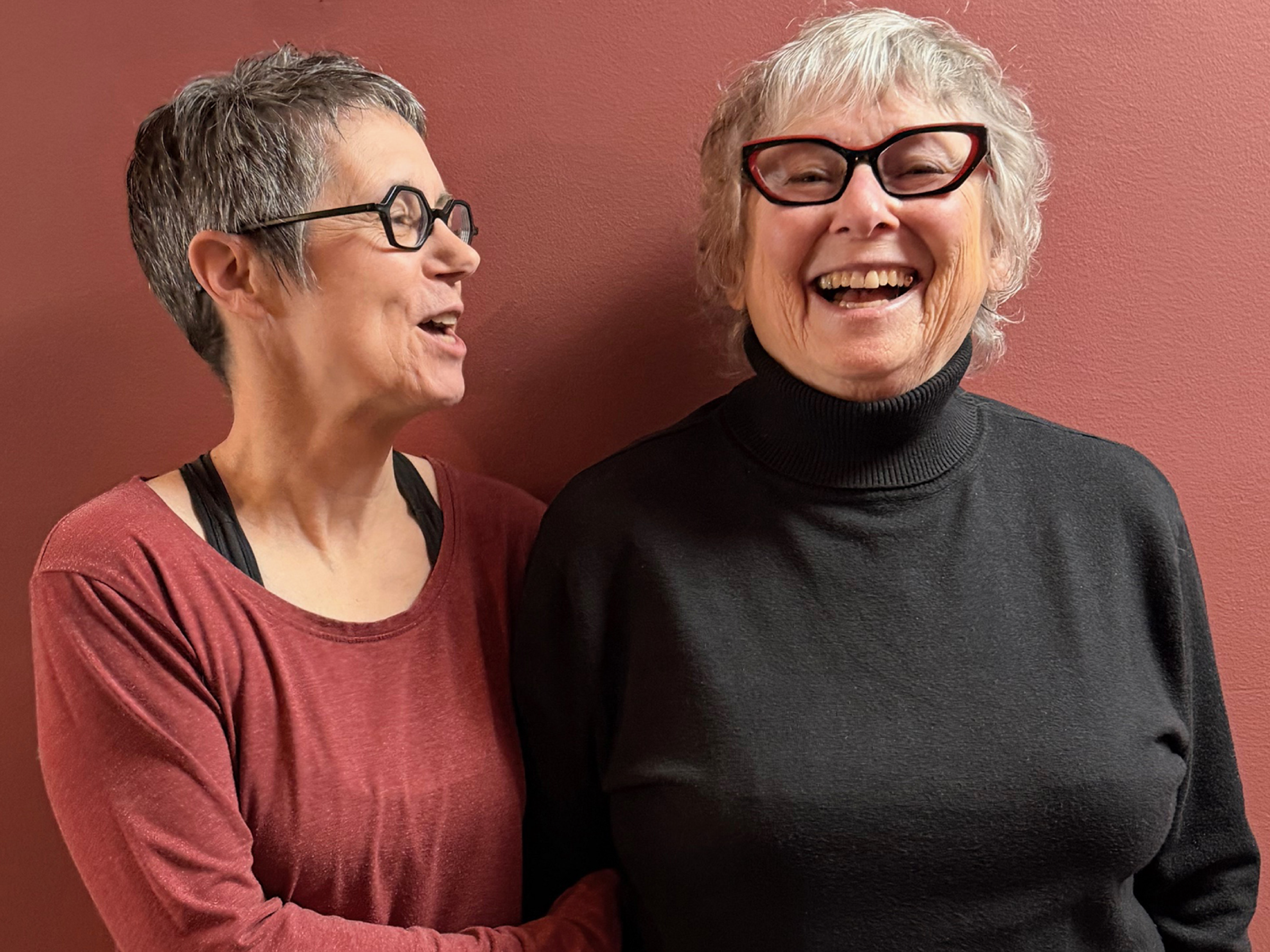 Reva Stone and Diana Thorneycroft standing in front of a red wall.