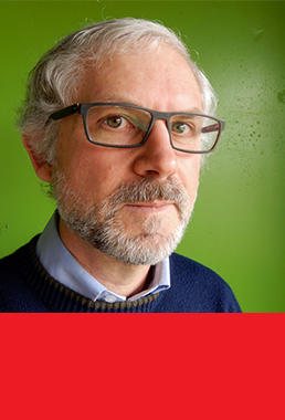 Man with gray hair and glasses in front of a bright green background