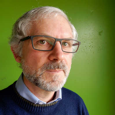 Man with short grey hair and glasses standing in front of a bright green backdrop