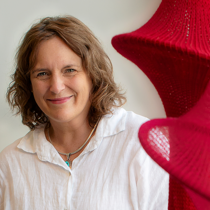 Woman with short wavy brown hair looking at the camera. Red crochet hanging to her left.