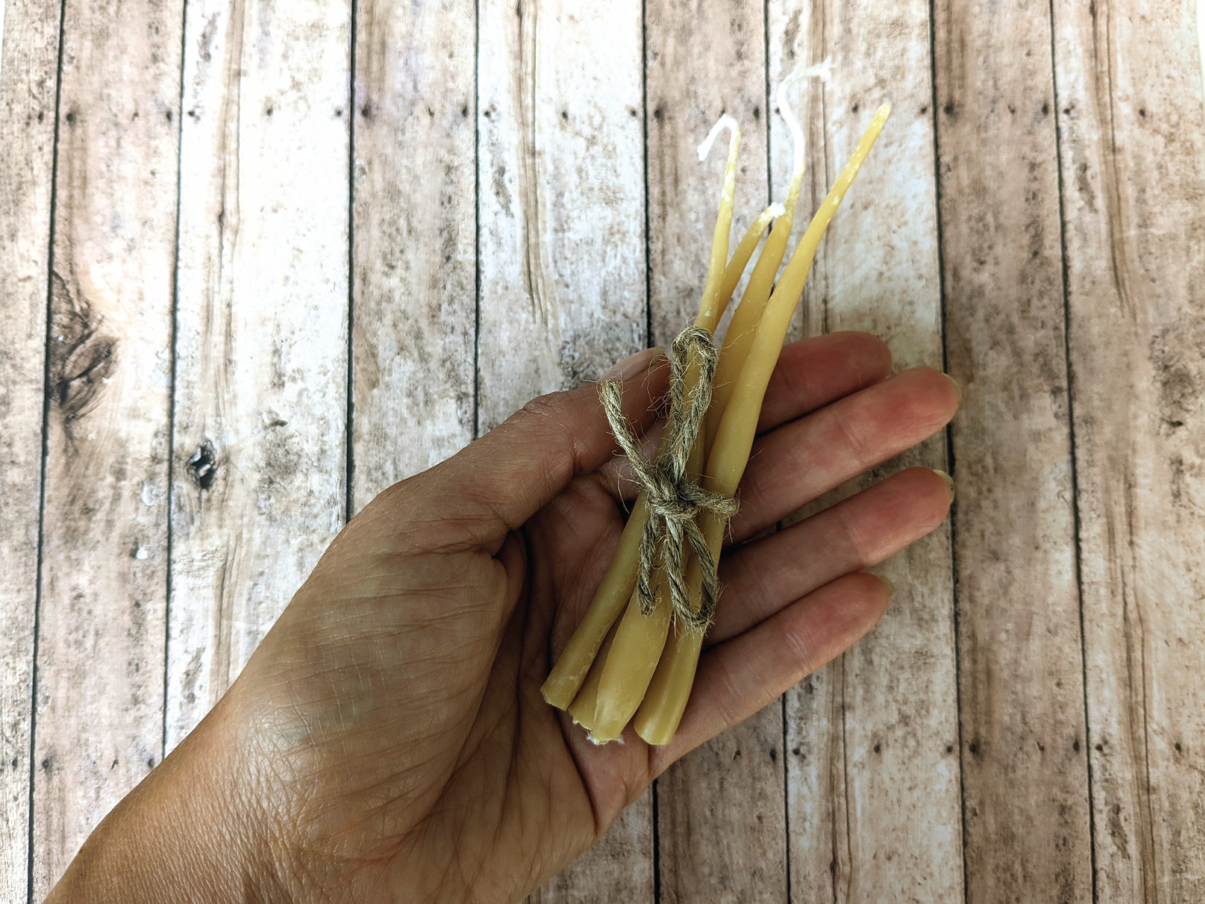 A hand holds out four small wax candles. The background is a wood grain pattern.