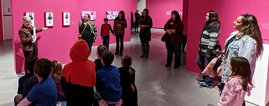 A woman talking to students in front of the Skawennati exhibition