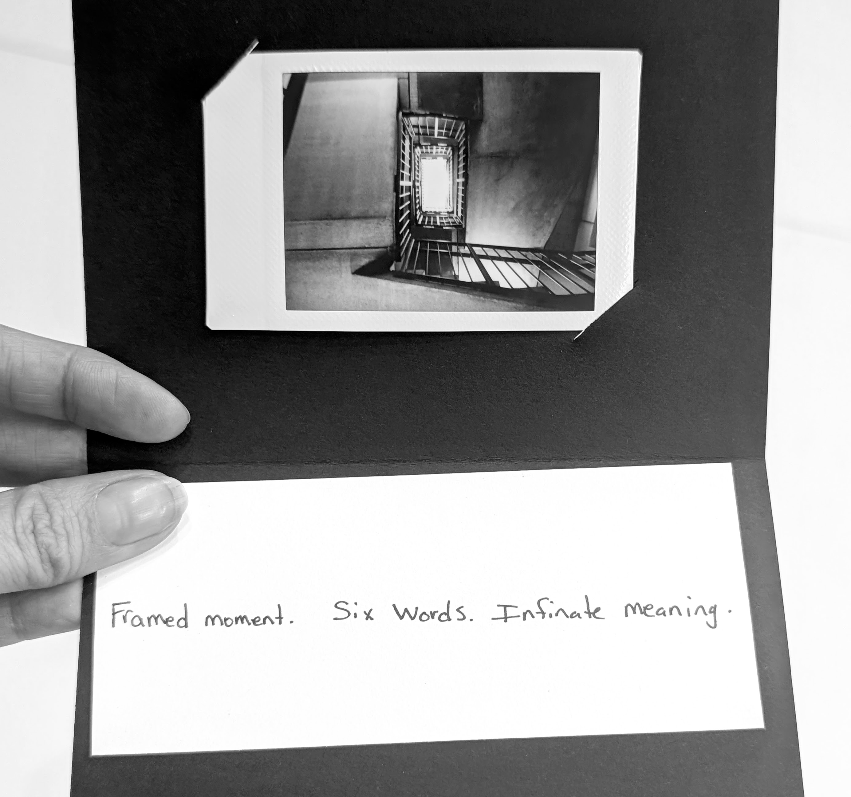 A black-and-white photo of a stairwell inside a card with handwritten text below reading "Framed moment. Six Words. Infinite meaning."