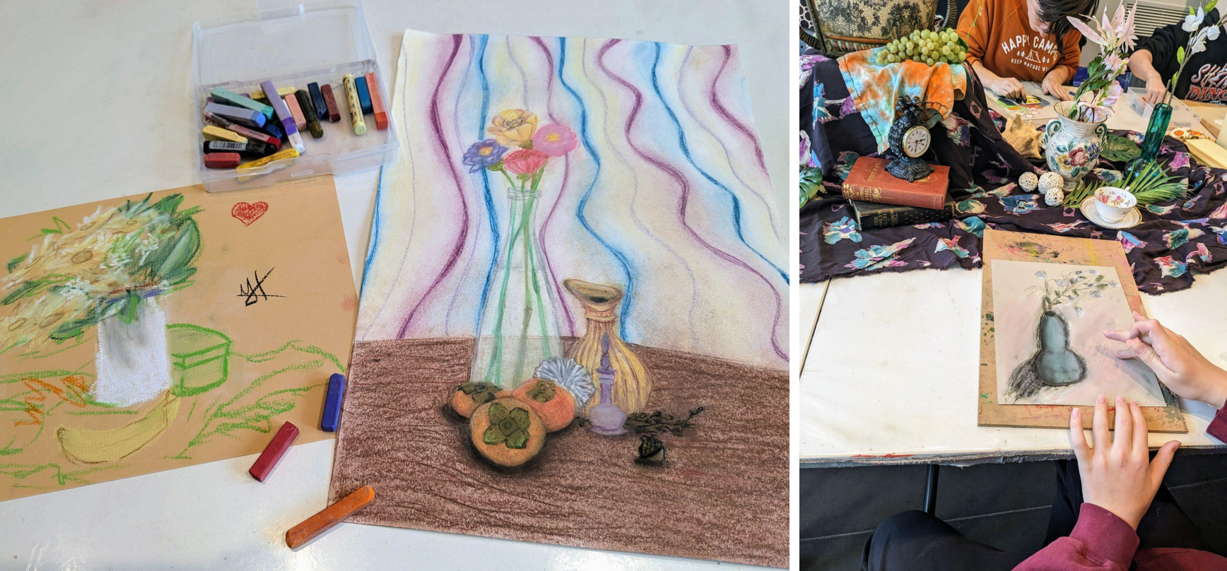 Soft pastel still life drawings beside a tabletop arrangement of flowers, fruit, books, and decorative objects.
