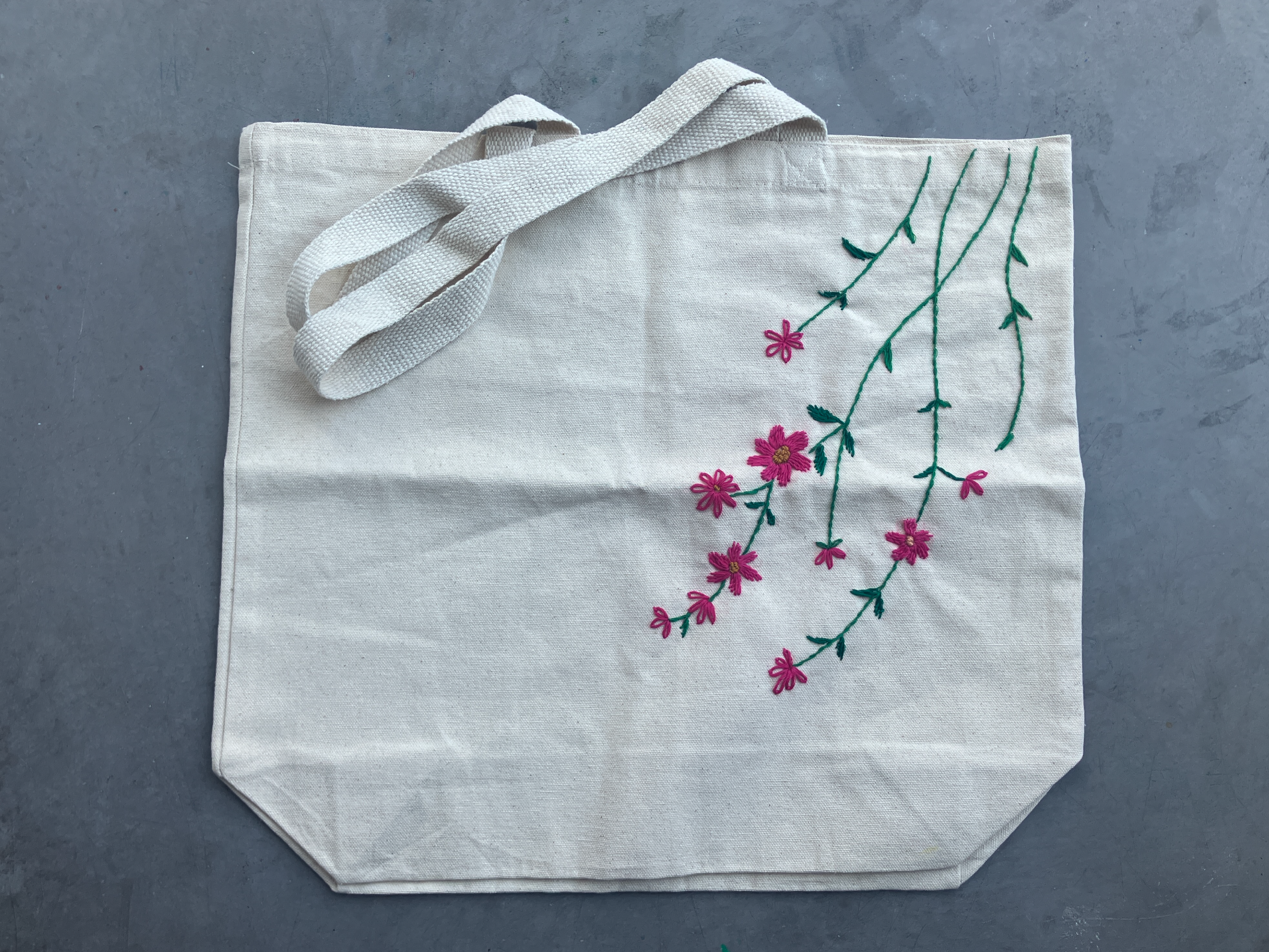a canvas tote bag highlights embroidered pink flowers and green stems.