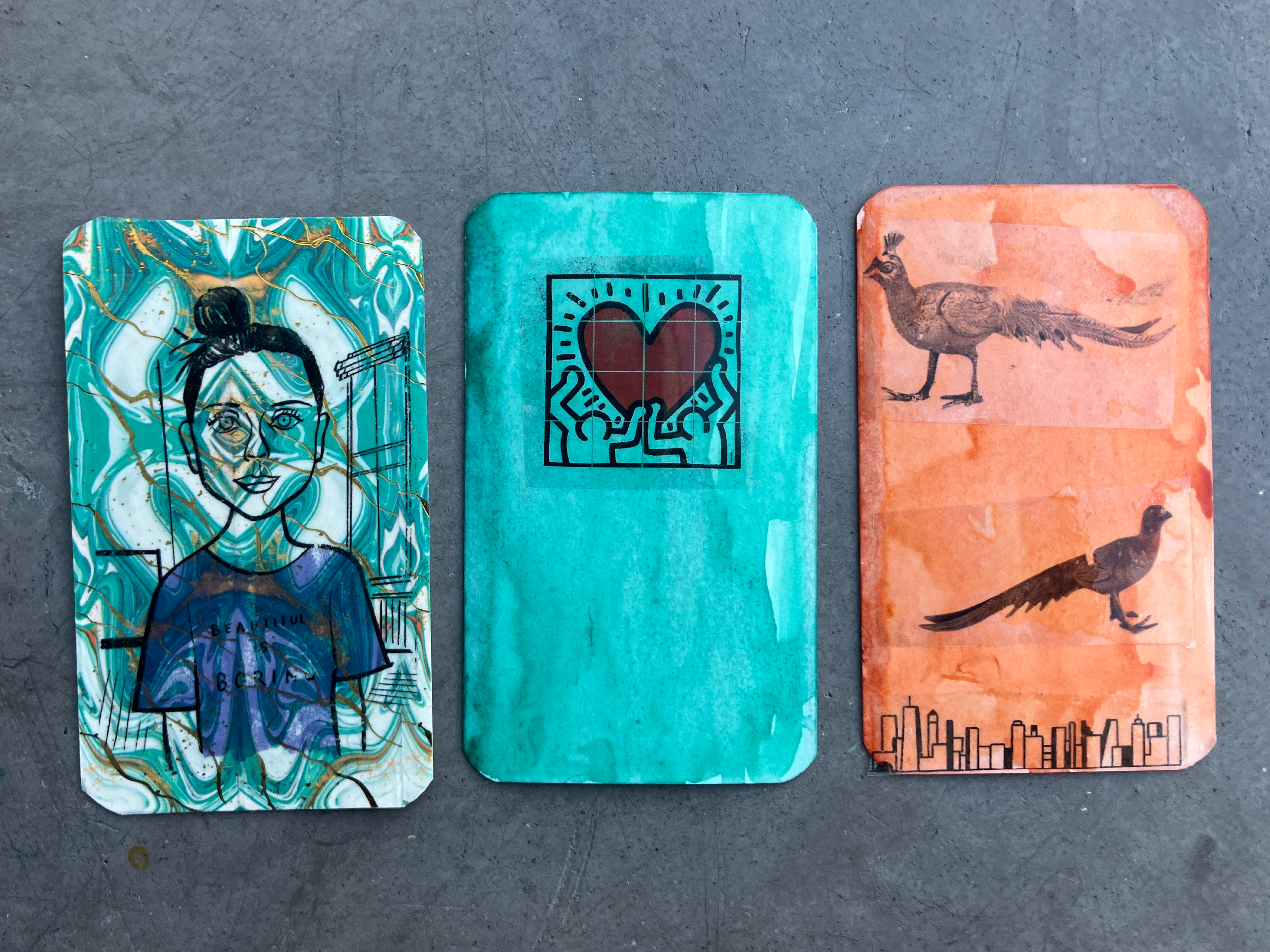 Three handmade trading cards sit on a grey tabletop.