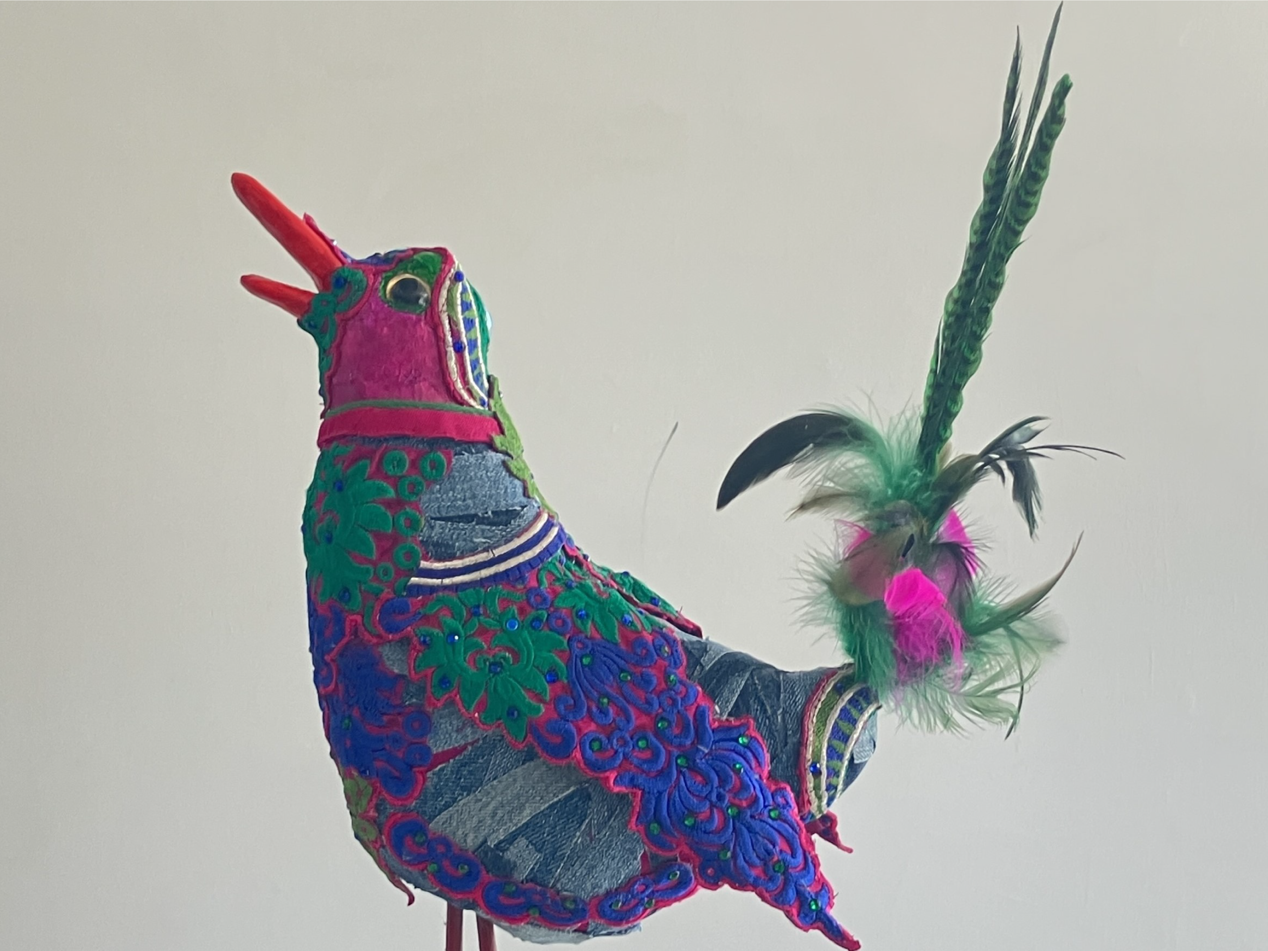 A bird sculpted from various textured fabrics on a white background