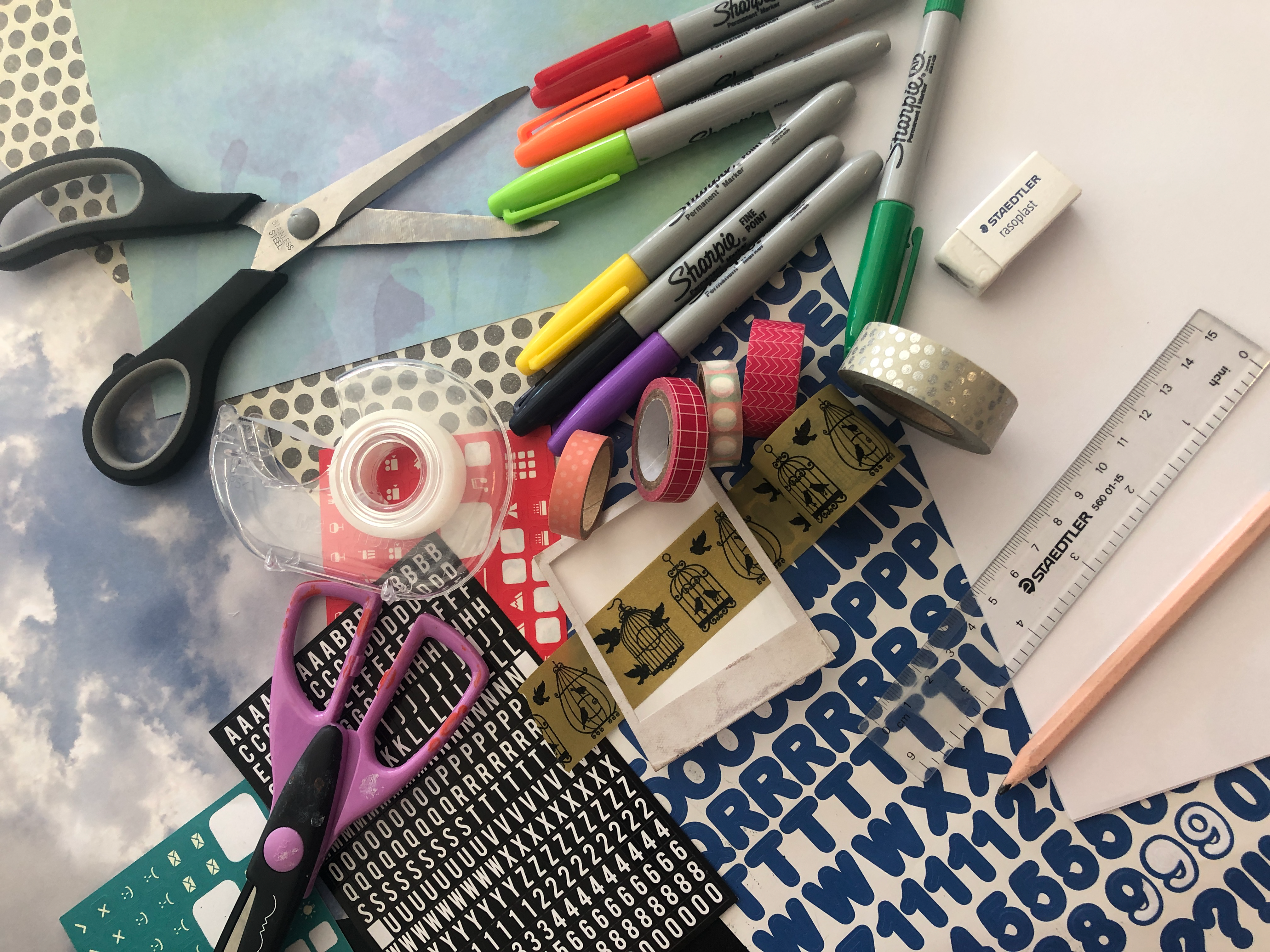 Assorted craft supplies including markers, scissors, stickers, tape, and patterned paper.