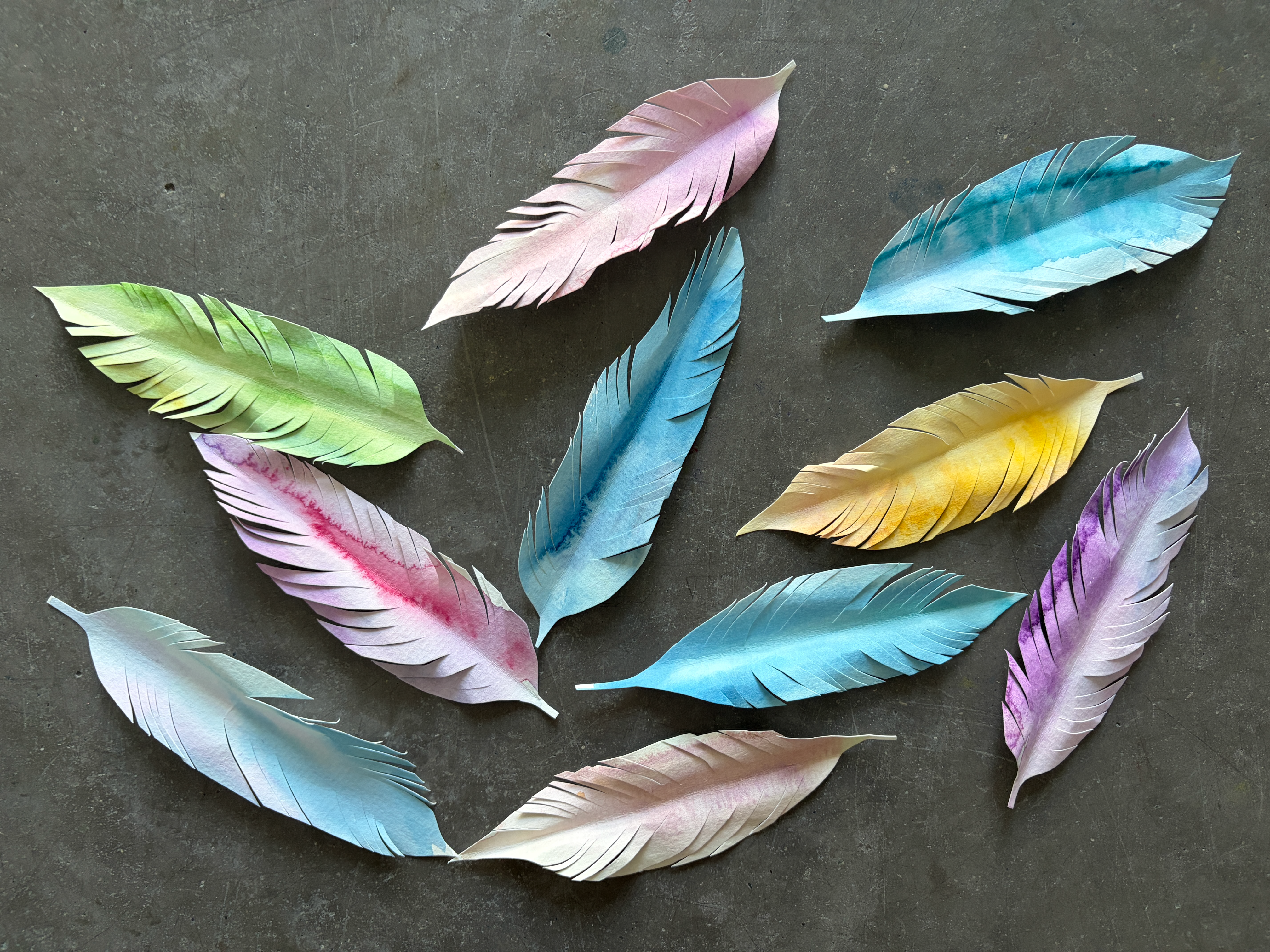 Coloruful paper feathers arranged on a tabletop in pastel shades of blue, pink, green, and yellow.