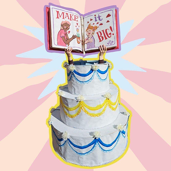 White layered cake with hands coming out of the top tear holding a book with word Make It Big printed on it