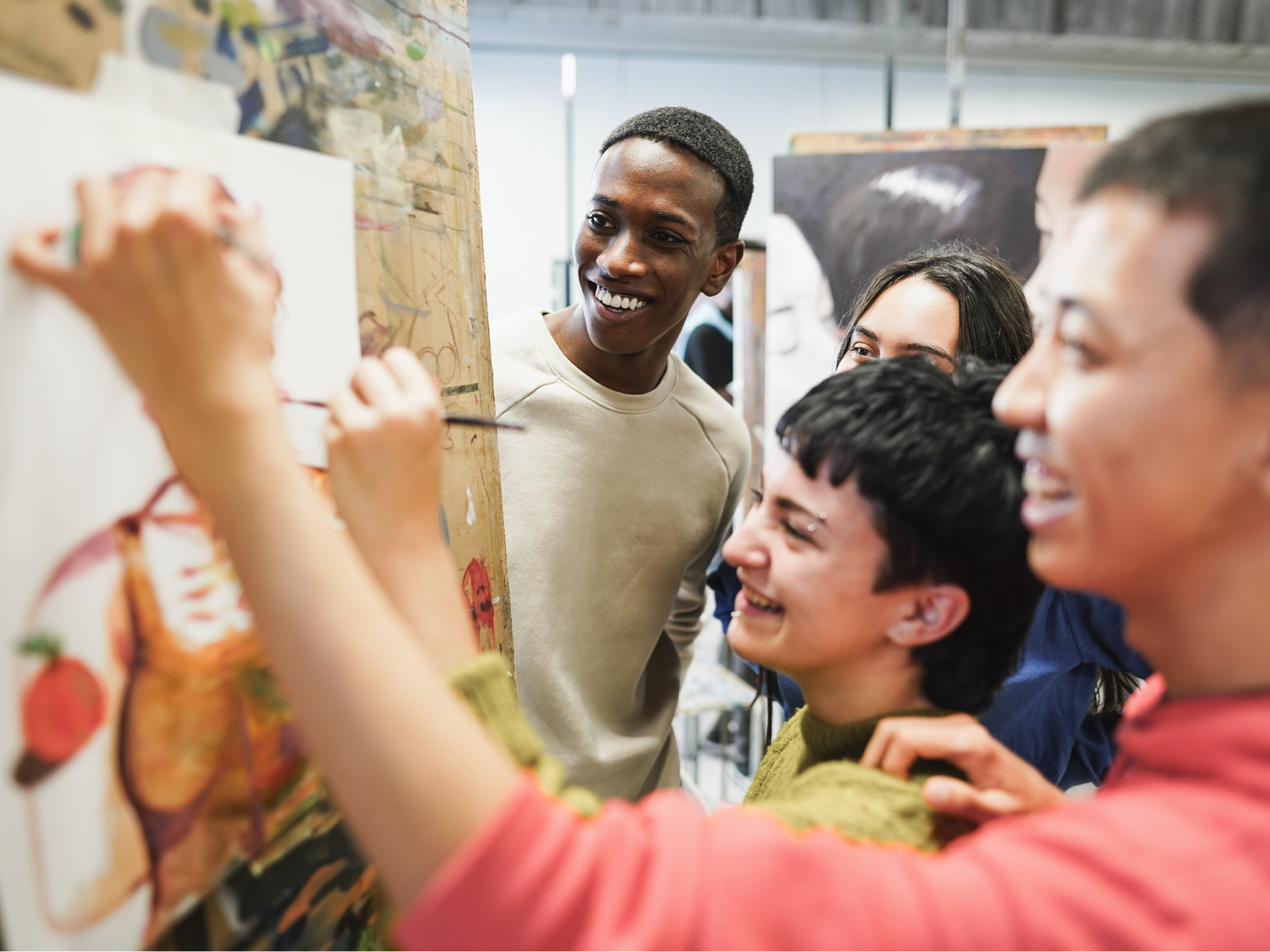 A group of people gathered around an easel, collaborating on a painting in an art classroom.