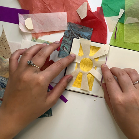 Two hands gluing a sun shaped cutout into a small binded book