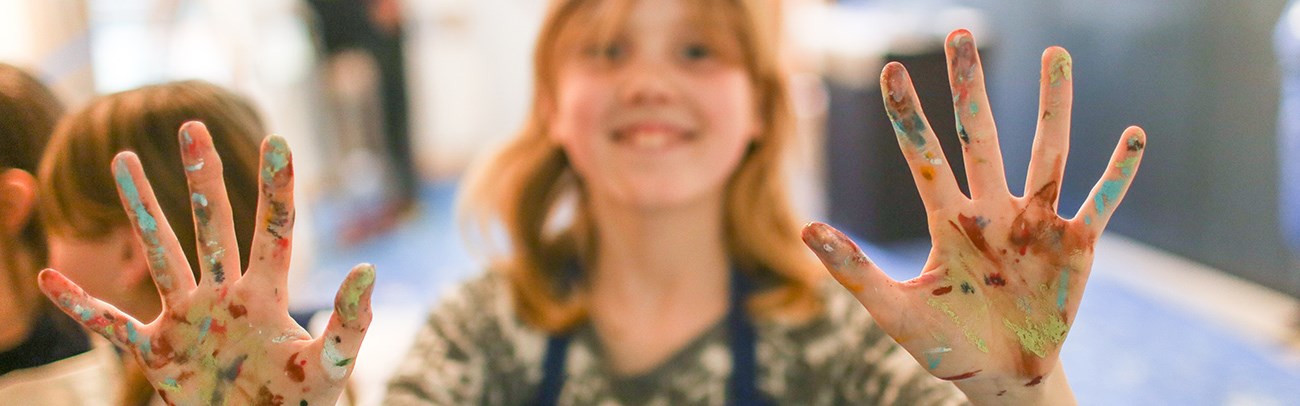 Girl showing paint on her hands while attending a family art program at the art gallery