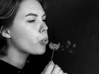 Humans of Lambton candid/environmental winner. A young girl makes a wish on a dandelion. The photo is shot in black and white.