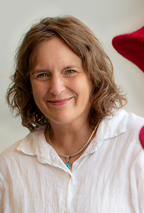 Woman with short wavy brown hair looking at the camera. Red crochet hanging to her left.