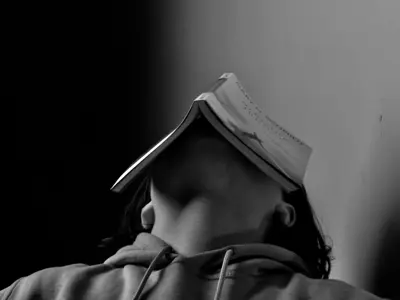 Feels Like Home people winner. A young boy sits with his head hung back and a book sitting atop it. The photo was taken in black and white.