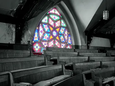 Lambton Through the Lens romance and ruin winner. An abandoned church pew area in black and white. The stain glass window in the background is highlighted in full colour.