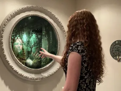 Humans of Lambton creative/fine art winner. A young girl holds her hand out to a mirror that appears to be a portal to a magical world.