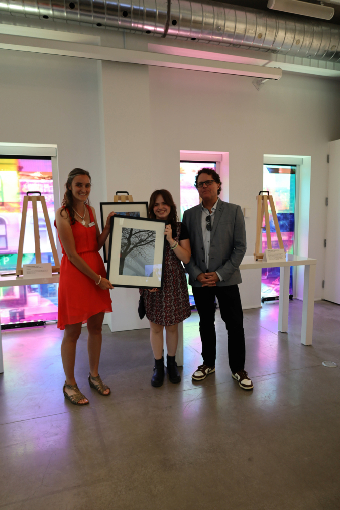 Isis Belleman-McKeegan (center) is awarded the grand prize for the 2024 Teen Photo Contest by Vanitia Campbell (left) and Richard Beland (right)