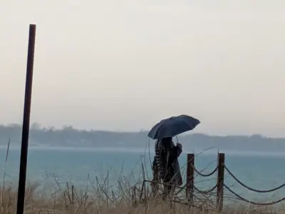 Stories In Focus drama winner. Two people stand under an umbrella on the beach, staring out into the lake.