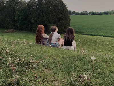 Humans of Lambton groups winner. Three young girls sit on a grassy hill with their backs facing the camera.